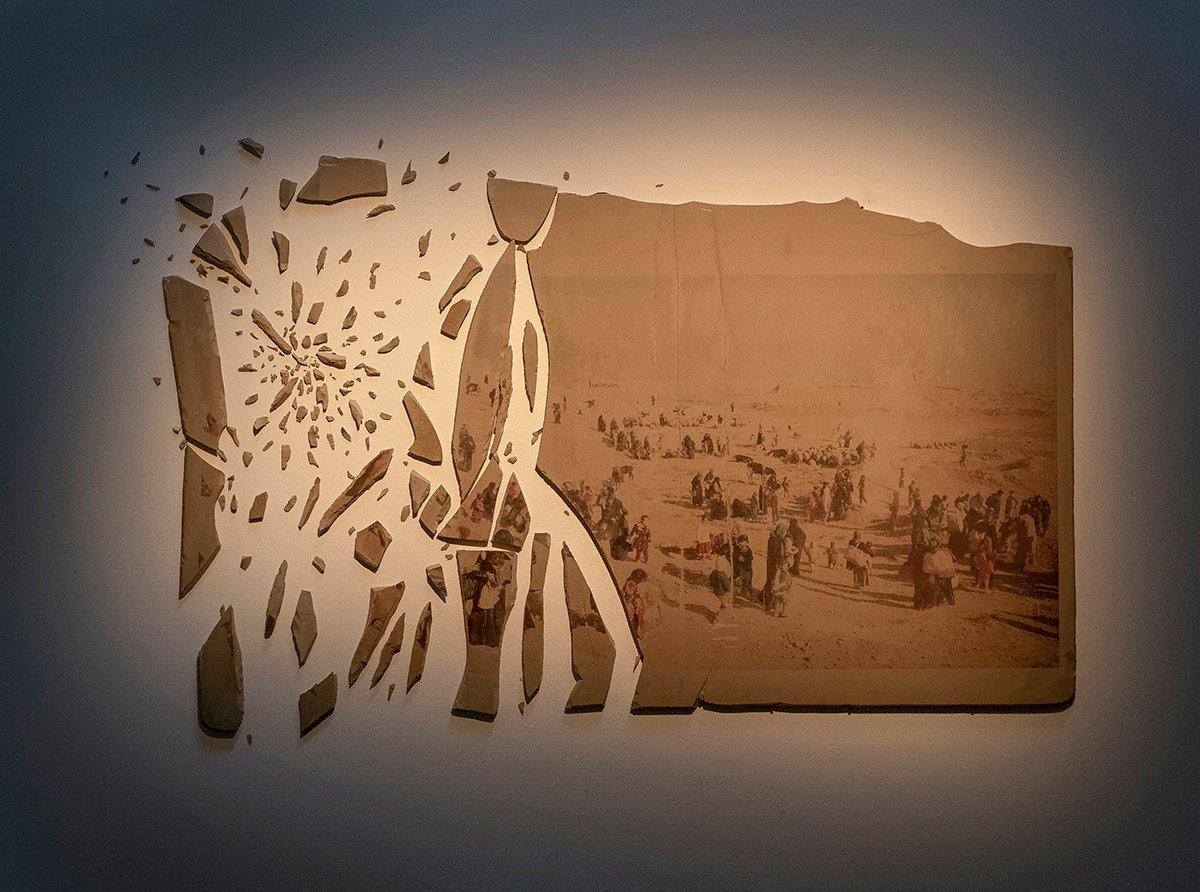 A broken monolithography stone by Ali Arkady, showing a photographic image of displaced people across the fractured surface.