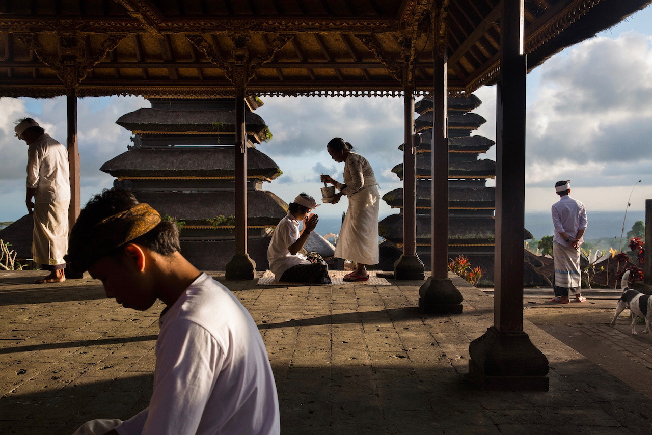 Worshippers in white move through the open pavilions of Besakih temple at dusk, Bali