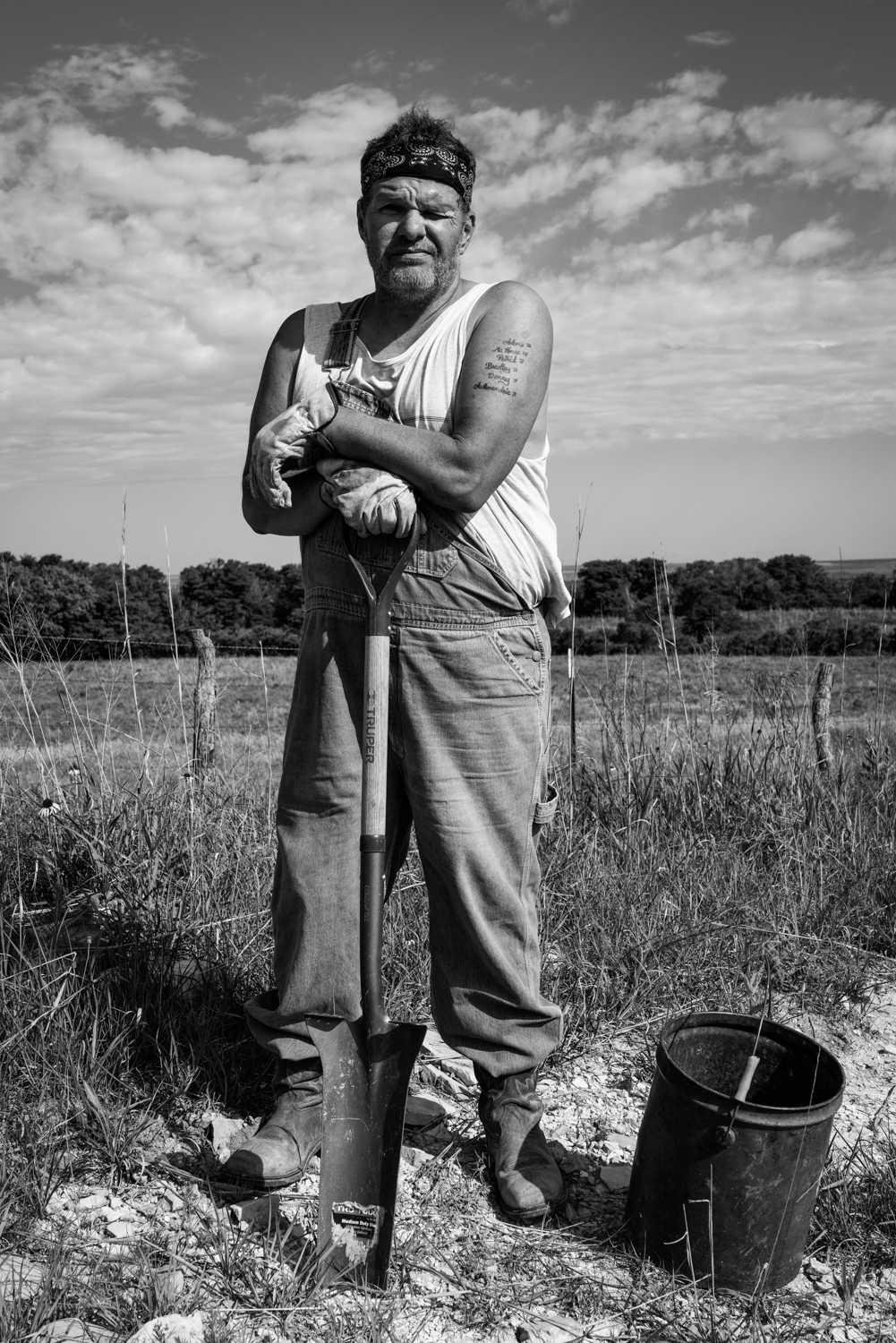 Man in overalls leaning on a shovel on the roadside, Kansas